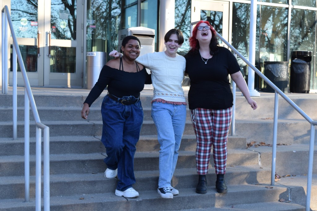 Three undergraduate students smile and laugh on the west steps outside Ekstrom Library with their arms around each other