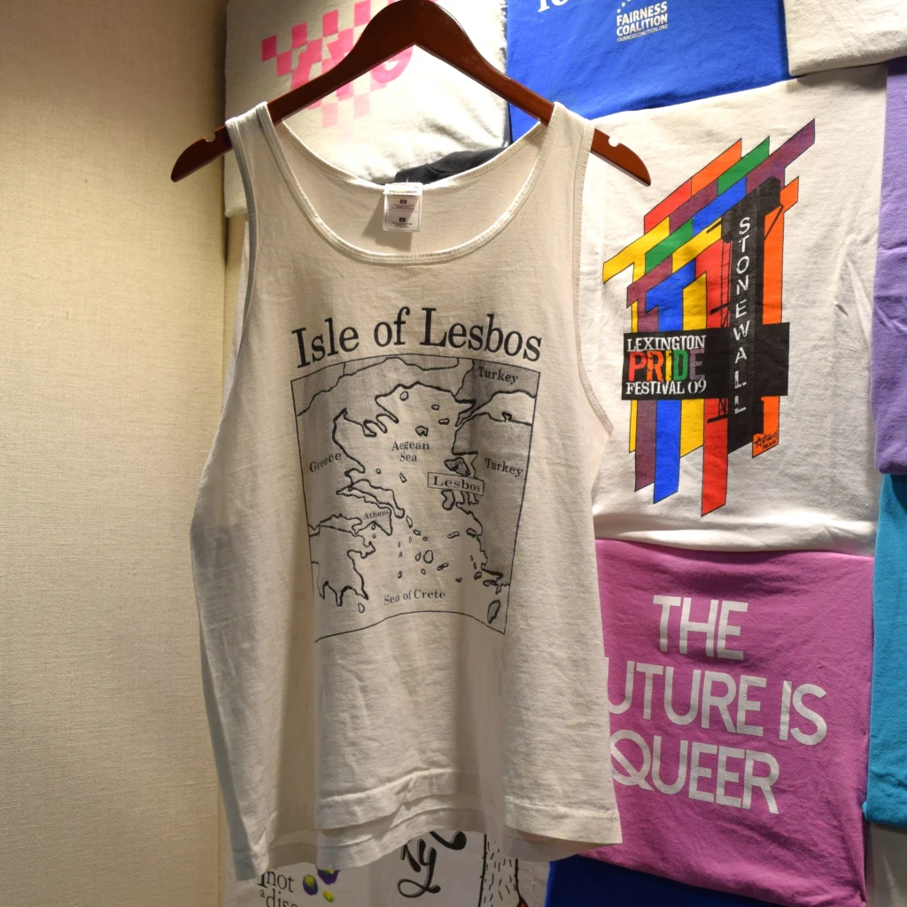 The famous 'Isle of Lesbos' shirt hangs in front of a colorful display of t-shirts from various LGBTQ+ movements across Kentucky.